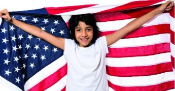 Jovencita posando, cubriéndose con la bandera de EE.UU. en fondo blanco