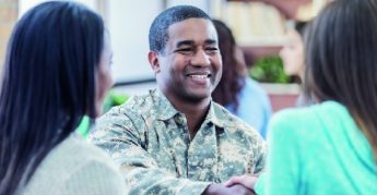 Smiling man in military uniform greeting 2 women. 