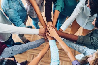 Image of  group of people standing in a circle with their hand piled up on each others in the middle of the circle.