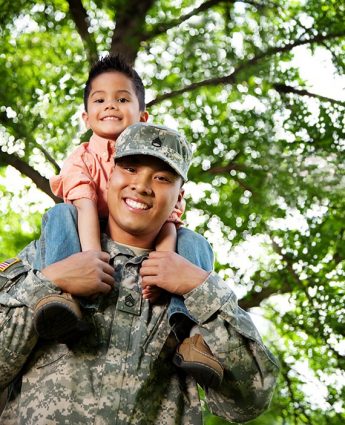 Closeup of Armed Force man with son on shoulder under a tree