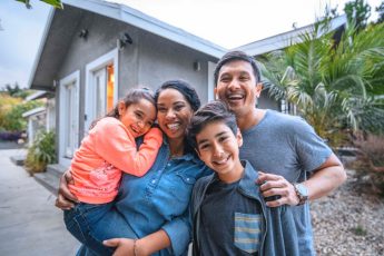 Una familia de cuatro personas posando para una foto en frente de su casa.