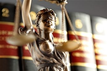 Lady justice holding balance scales in front of a book shelf full of law books