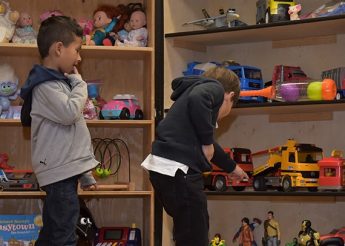 Two boys looking through a shelf with toys.  