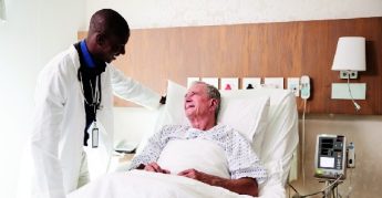 Doctor visitando y hablando con paciente masculino de mayor de edad (60 o más) en la cama del hospital.