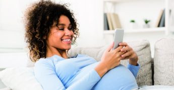 Mujer embarazada sonriente sentada en el sofá usando el teléfono celular.