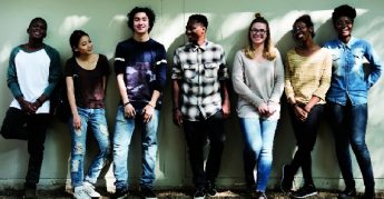 Several teens smiling standing against a wall