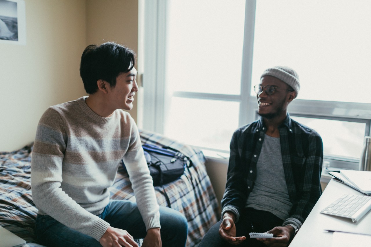 African american and asian men chatting in a dormitory room.