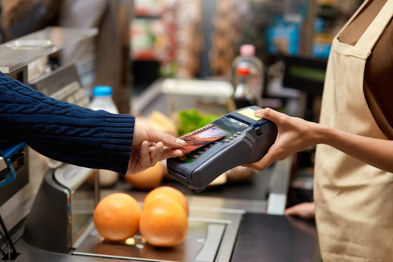 Customer is paying at checkout line of the grocery store by tapping Golden State Advantage card against credit card terminal.