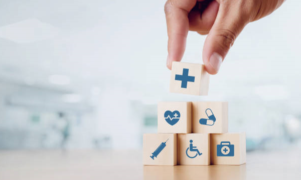 A picture of a hand of a person stacking multiple wooden blocks with different medical services related symbols.