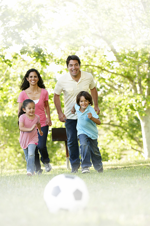 Young Hispanic Family Having Fun Playing Football Outside In Park