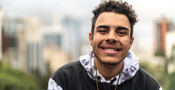 Young male smiling outside with city in the background