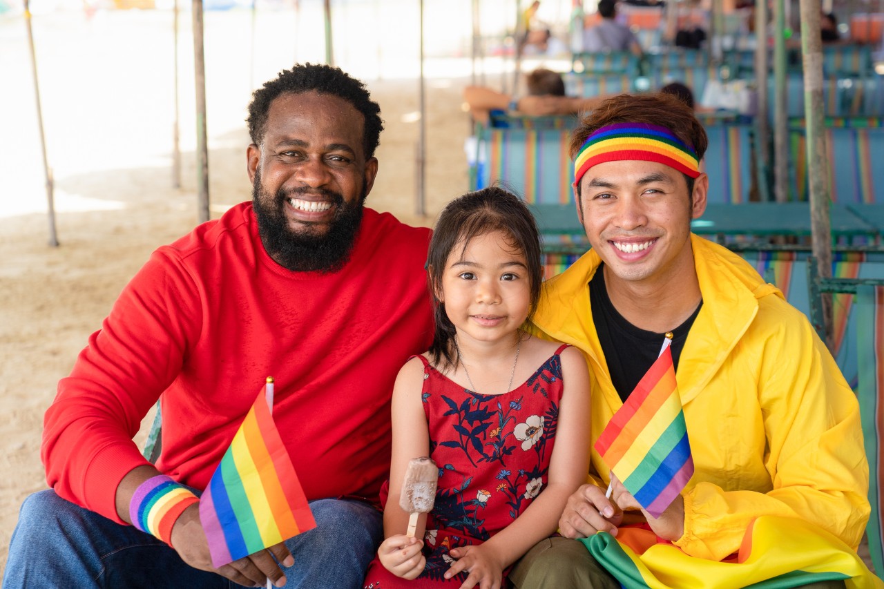 Gay couple family with child smiling during summer day in pride month.
