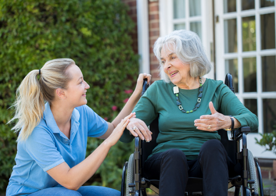 Caregiver Pushing Senior Woman In Wheelchair Outside Home