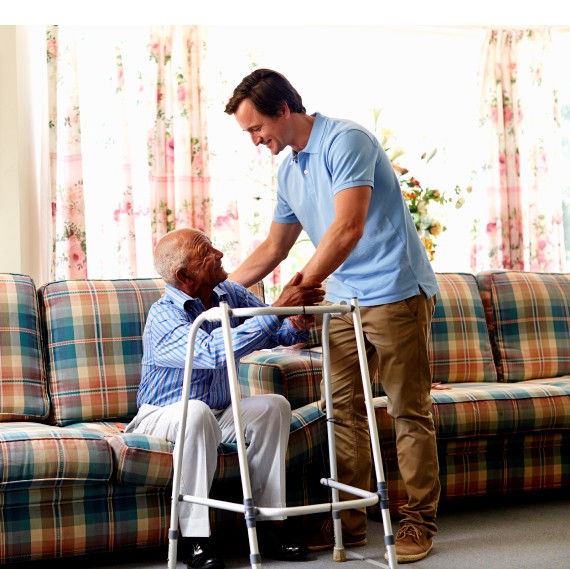 Male caretaker helping senior man with walker in nursing home