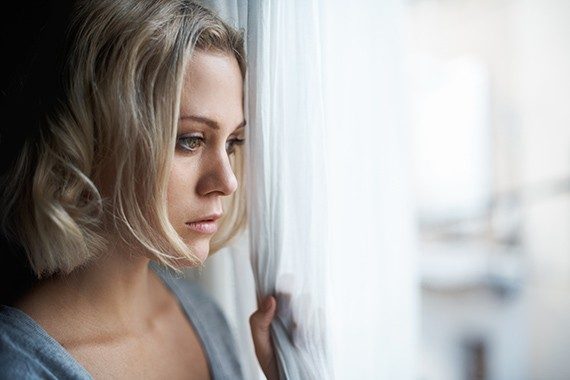 Una hermosa joven rubia mirando por la ventana con tristeza