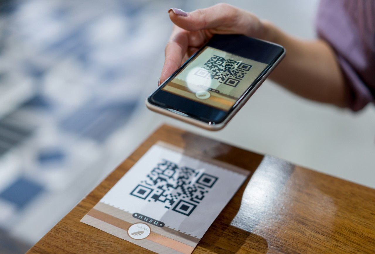 Primer plano de una mujer escaneando un código QR para obtener el menú en un restaurante. **CÓDIGO QR WA